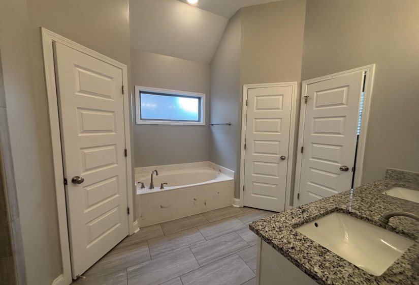 Bathroom featuring a built-in tub, a window above the tub, two panel doors, a double vanity with undermount sinks, and stone-finish countertops