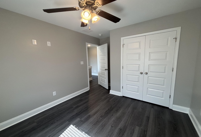 Bedroom featuring wood-finish flooring, light gray walls, a ceiling fan with integrated lighting, and white bi-fold closet doors