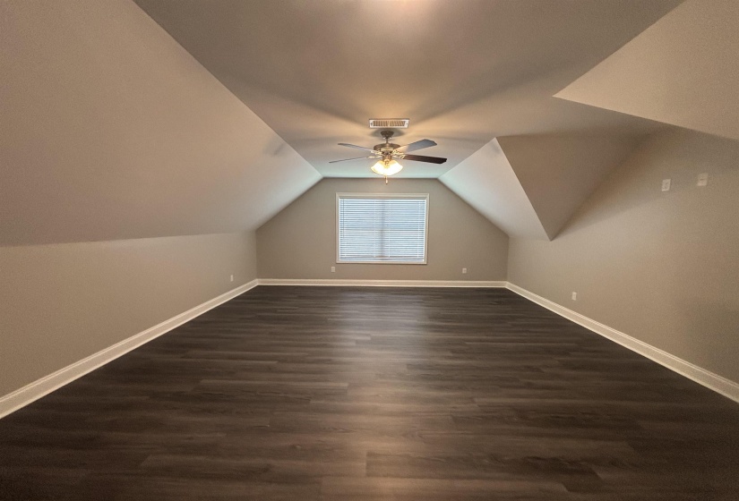 Spacious room featuring vaulted ceilings, dark wood-finish flooring, and a ceiling fan with integrated lighting