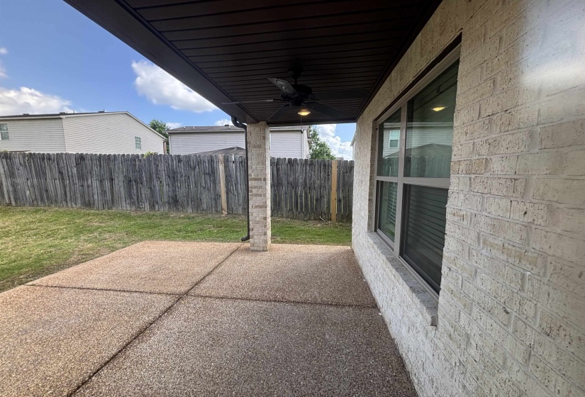 Covered patio featuring an exposed aggregate concrete surface, a brick column, and a ceiling fan with integrated lighting