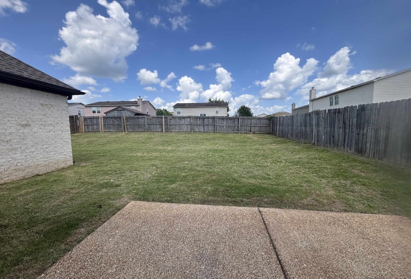 Expansive backyard featuring a large grass lawn, perimeter wood fencing, and a concrete patio
