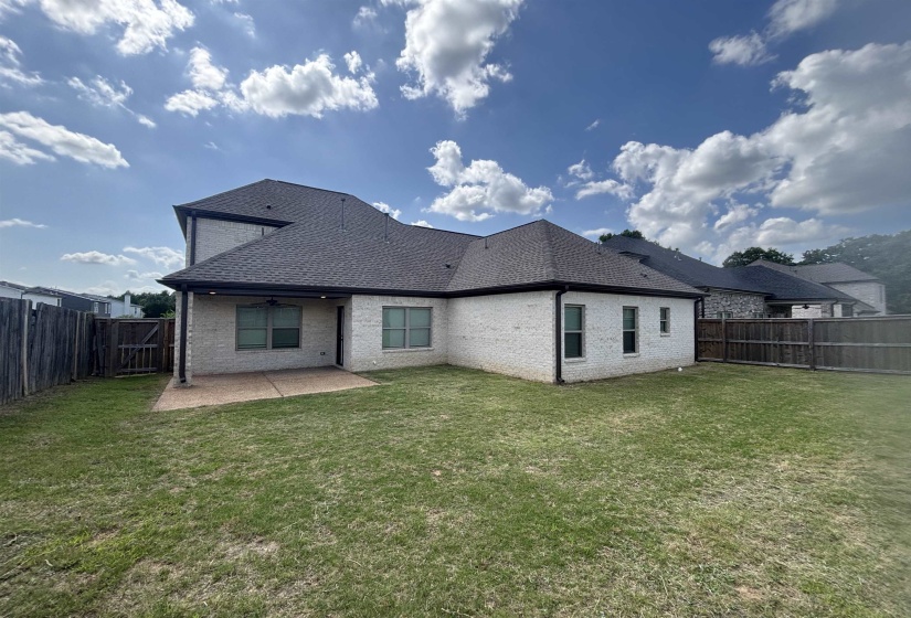 Expansive backyard featuring a manicured lawn, full privacy fencing, and a large concrete patio with an overhead fan and recessed lighting