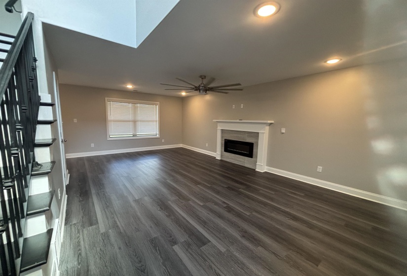 Spacious interior with wood-finish flooring, a built-in electric fireplace with a white mantel, and a multi-blade ceiling fan