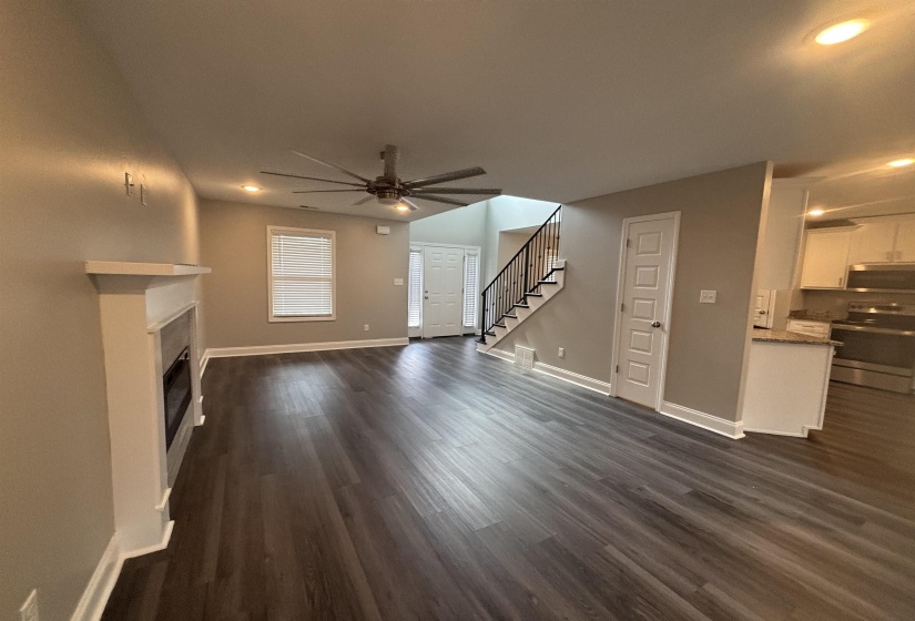 Spacious living area featuring wood-finish flooring, a white mantel fireplace, a large ceiling fan, and recessed lighting