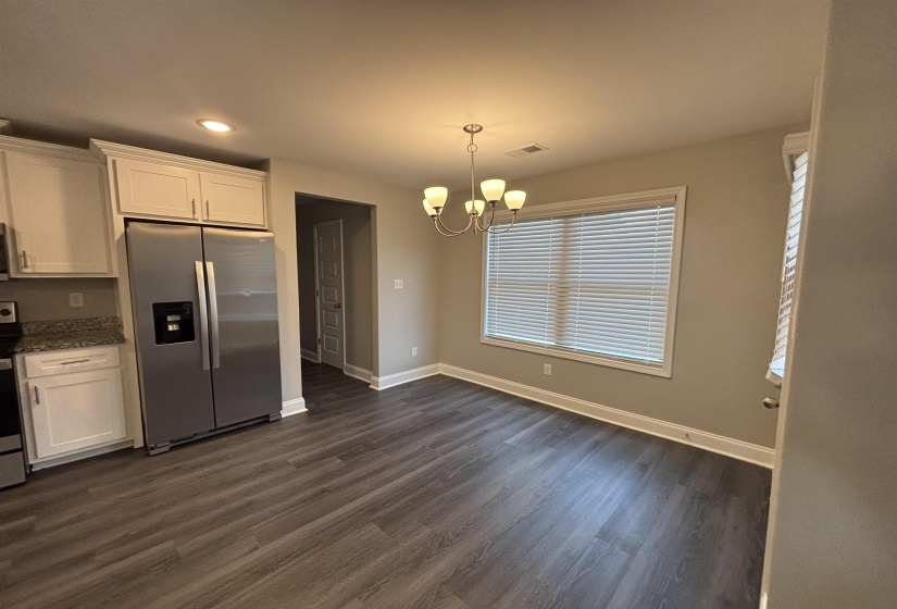 Open-concept living space featuring wood-finish flooring, a stainless steel refrigerator, white cabinetry, granite-look countertops, and a window with blinds