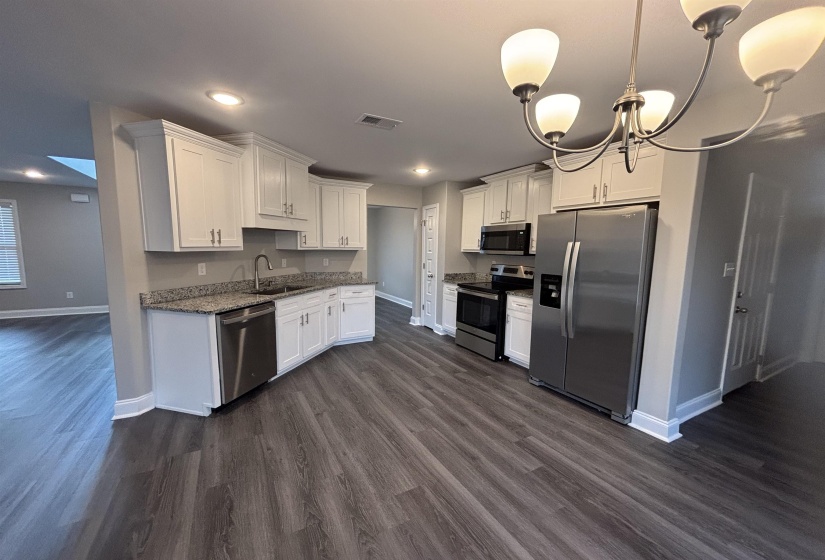 Modern kitchen featuring white cabinetry, granite-style countertops, stainless steel appliances, wood-finish flooring, and a contemporary chandelier