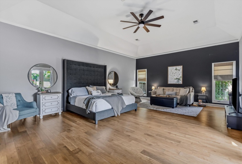 Spacious room featuring wood-finish flooring, a tray ceiling with a dark ceiling fan, and accent wall