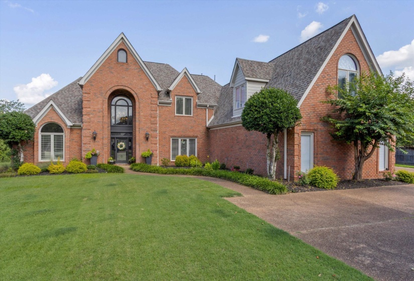 Brick exterior featuring multiple gables, arched windows, an arched entry, a shingle roof, and a mature landscaped lawn