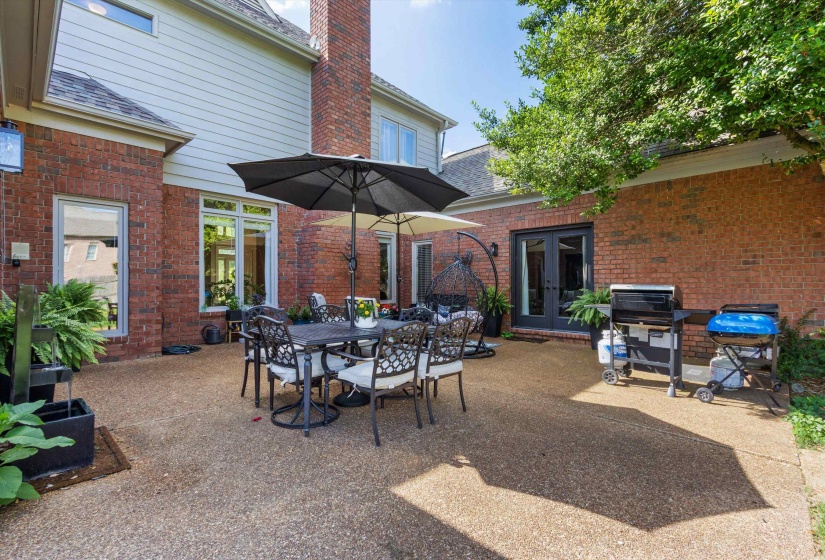 Expansive brick patio featuring a textured concrete surface, multiple windows, double French doors, and mature landscaping