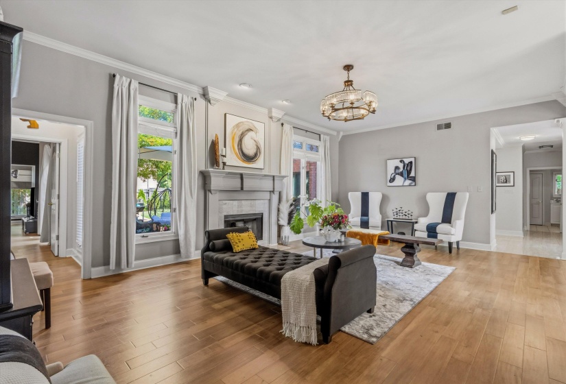 Spacious living area featuring wood-finish flooring, a traditional fireplace with a mantle, and crown molding
