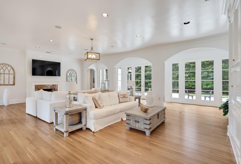 Spacious living area featuring light wood-finish flooring, a fireplace with a stone surround, and multiple sets of French doors with arch top transoms