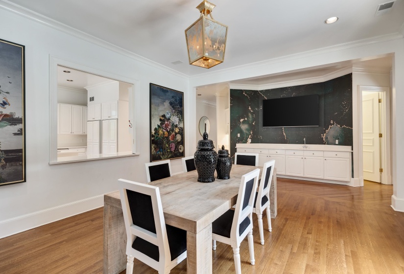 Warm wood-finish flooring complements a built-in wet bar with white cabinetry and dark, veined wall paneling