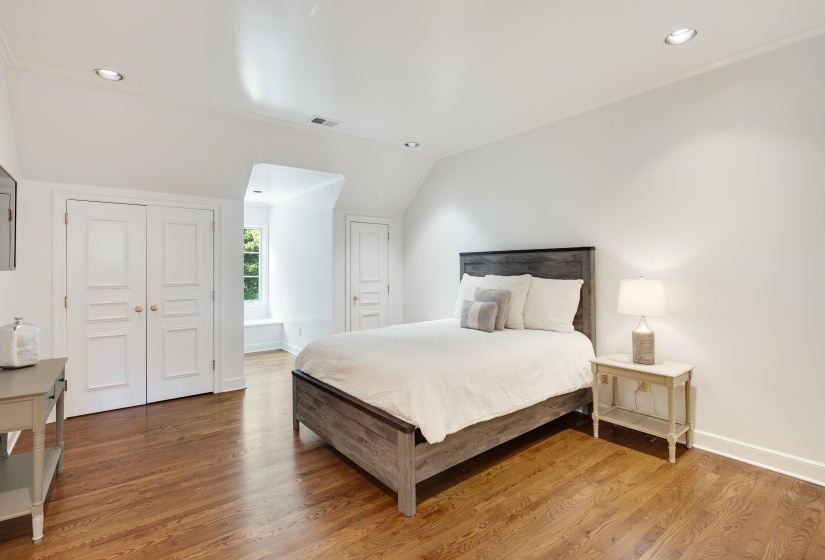 Spacious room featuring wood-finish flooring, white walls, recessed lighting, and a window with a built-in bench