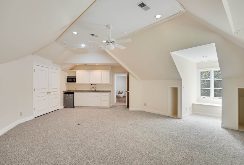 Spacious carpeted room featuring a built-in wet bar with white cabinetry, a window seat with natural light, sloped ceilings, recessed lighting, and a ceiling fan
