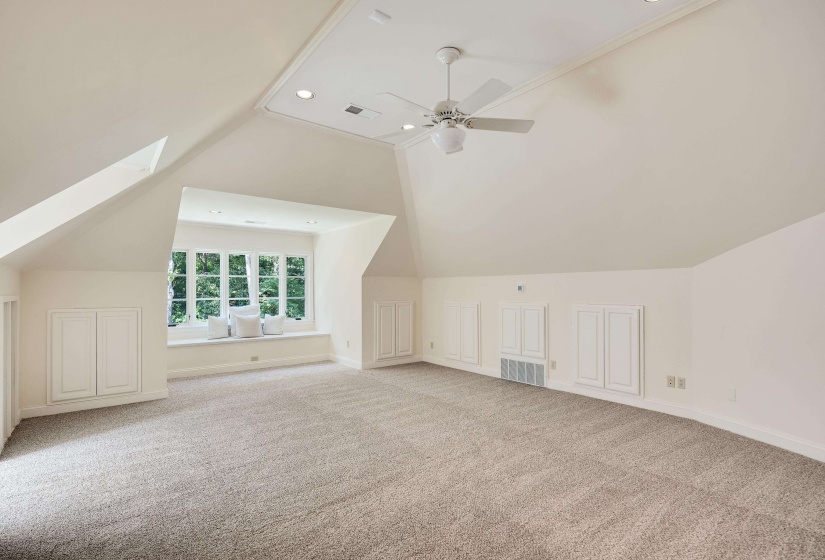 Spacious room featuring vaulted ceilings, neutral carpet flooring, a window seat with multiple pane windows, and built-in cabinetry with panel doors