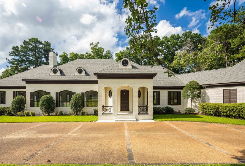 Stately residence featuring a light-colored brick exterior, dark trim accents, a prominent covered entry with an arched doorway, a multi-gabled roofline, and dormer windows