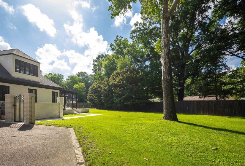 Expansive green lawn with mature trees, bordered by a wooden privacy fence