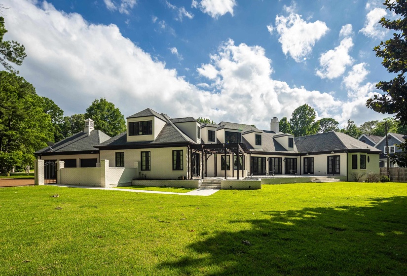 Expansive rear elevation featuring a stucco exterior, multiple dormer windows, a large patio, a pergola structure, and a lush lawn