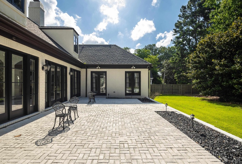 Expansive paver patio with a herringbone pattern, bordered by a black rock landscaping bed with integrated lighting