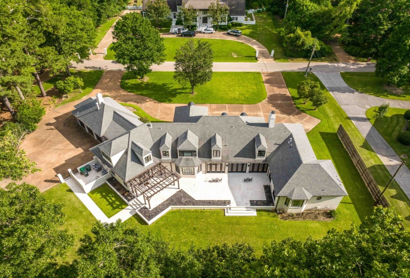 Expansive property featuring a multi-gabled roofline, a large paved patio, a pergola-covered outdoor area, a manicured lawn, and mature trees