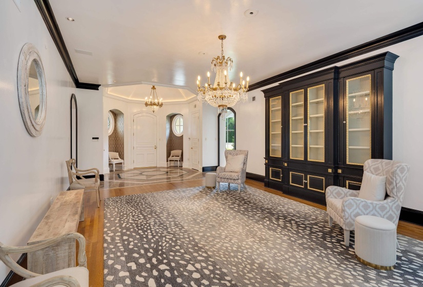 Grand foyer featuring a large crystal chandelier, integrated display cabinetry with glass doors, and a decorative tile floor inlay