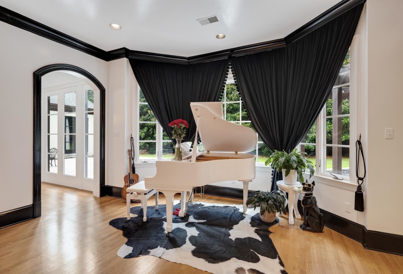 Hardwood flooring with a gloss finish, arched doorway with trim, French doors, recessed ceiling lighting, and black window treatments