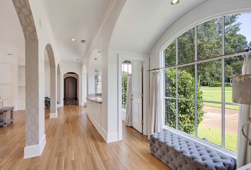 Grand foyer featuring a large arched window, natural wood-finish flooring, and a series of architectural archways