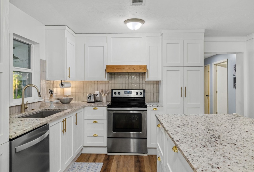Kitchen featuring white shaker cabinetry, stainless steel appliances, light granite countertops, a tile backsplash, and wood-finish flooring