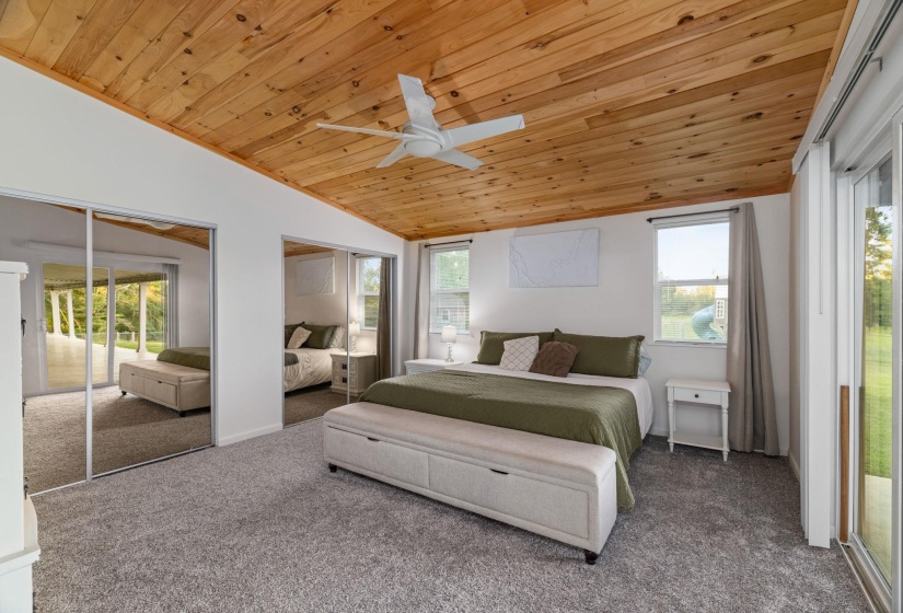 Vaulted wood-plank ceiling with a ceiling fan, plush grey carpeting, white walls, and mirrored closet doors