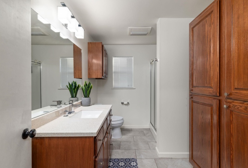 Bathroom featuring a wood vanity with a light-toned countertop, an integrated sink, a large wall mirror, and a multi-bulb vanity light fixture