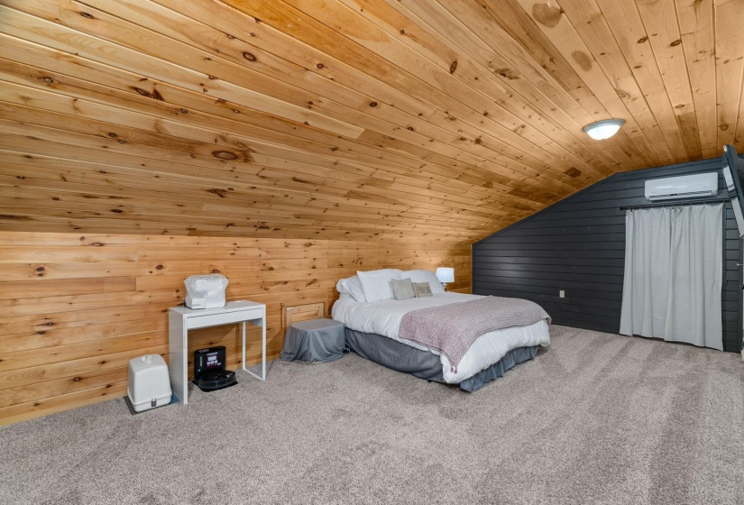 Sloped ceiling room featuring natural wood paneling, dark accent wall, and light grey carpeting