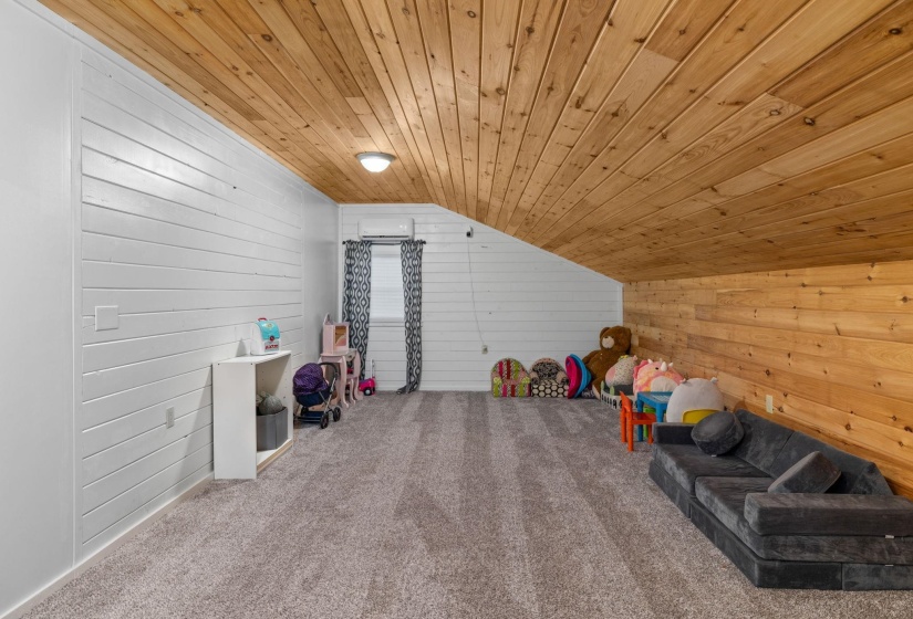 Spacious attic room featuring wood-finish plank ceiling, shiplap-style walls, and gray carpet flooring
