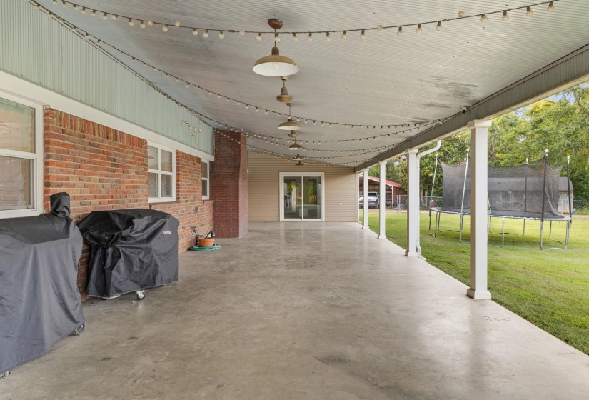 Expansive covered patio with concrete flooring, brick exterior wall, and white support columns