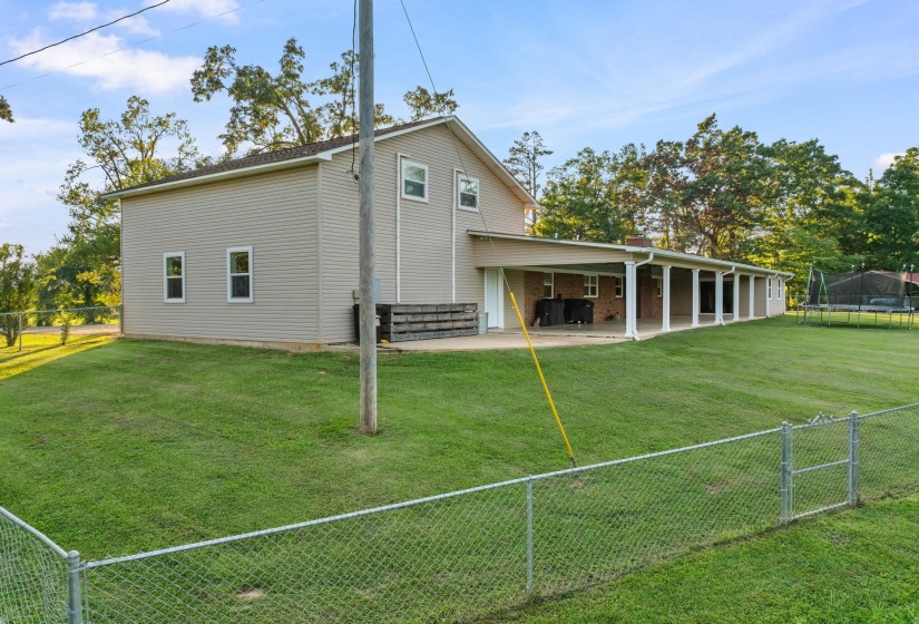 Expansive rear yard featuring green lawn, a chain-link fence, and mature trees