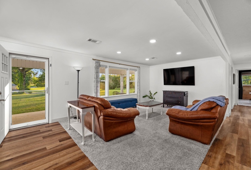 Living room featuring wood-finish flooring, recessed lighting, a large window providing natural light, and a white interior color palette