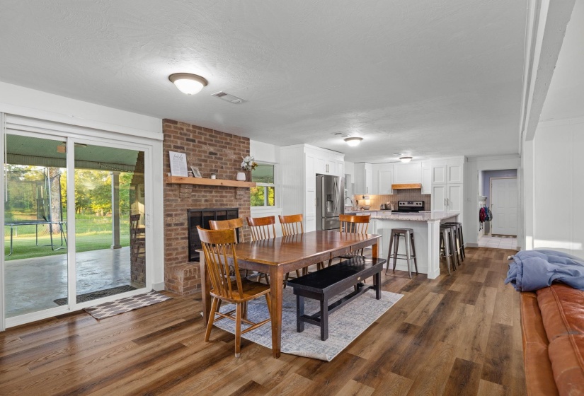 Spacious living area featuring wood-finish flooring, a brick fireplace with a wood mantle, and sliding glass doors opening to a covered patio