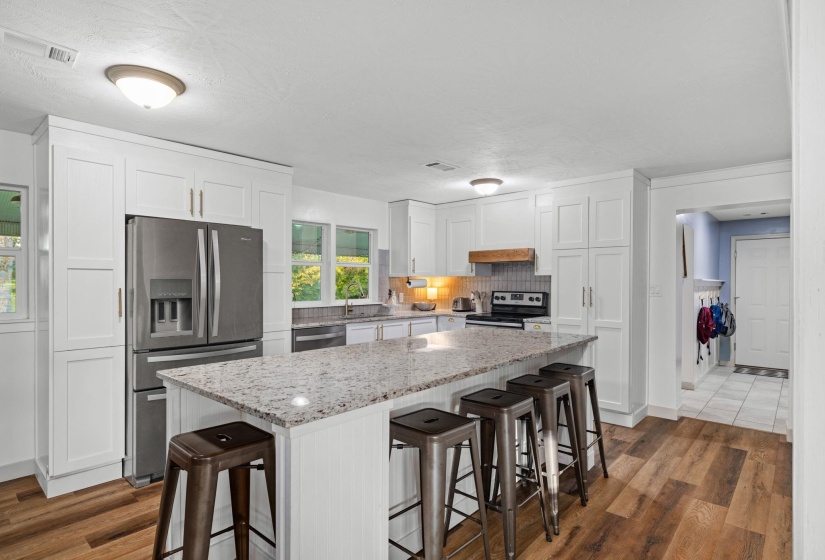 Kitchen featuring a central island with granite countertop, white shaker cabinetry, stainless steel appliances, and wood-finish flooring