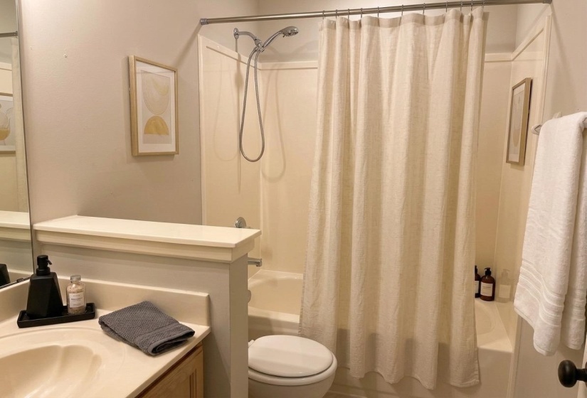 Full bathroom featuring a shower/tub combination with a showerhead, a toilet, a vanity with an integrated sink, and a large wall mirror