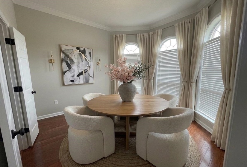 Dining area with hardwood-finish flooring, crown molding, and a bay window featuring arched transom windows and blinds
