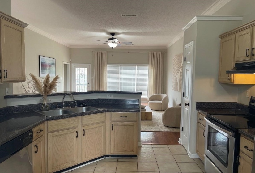 Kitchen featuring light wood-finish cabinetry, dark granite-style countertops, stainless steel sink, and tile flooring