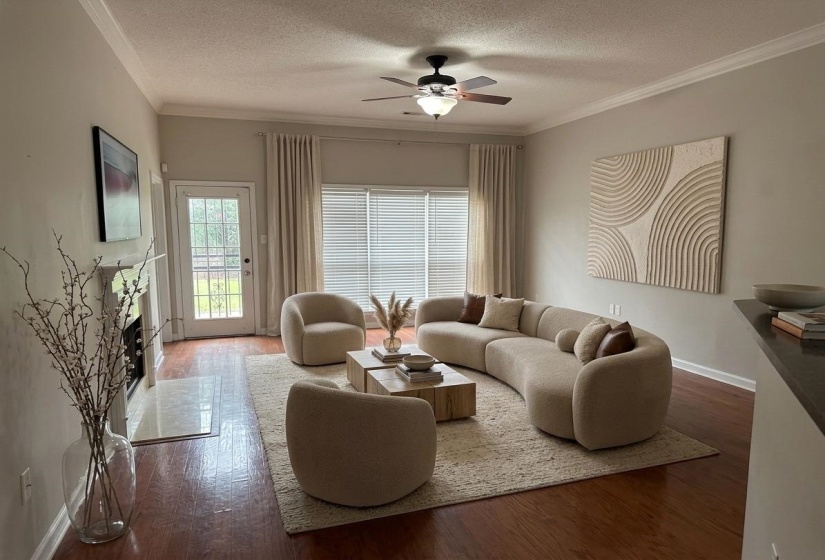 Living area featuring rich wood-finish flooring, a ceiling fan with integrated lighting, crown molding, and a fireplace with a light-colored hearth