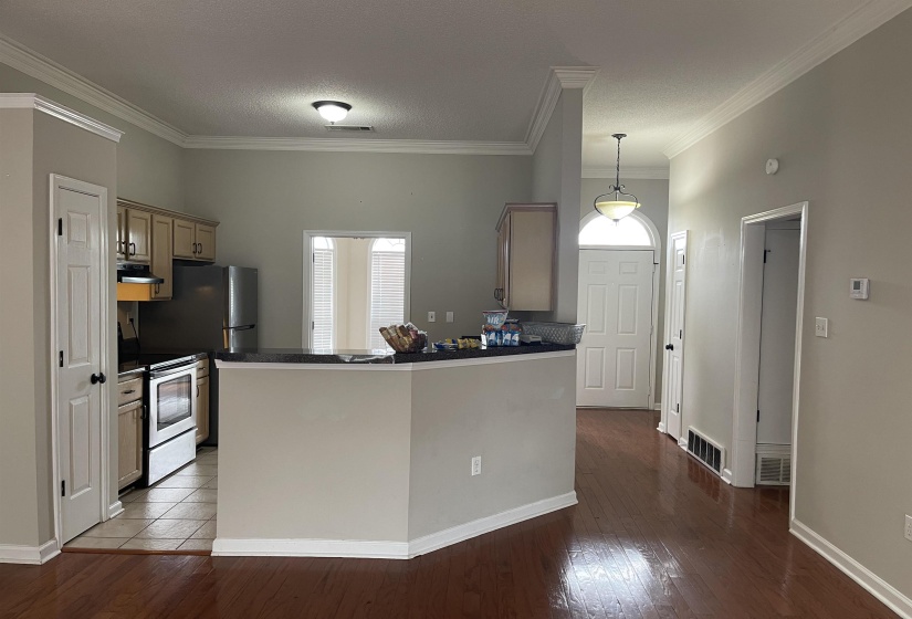 Open-concept living area featuring rich wood-finish flooring, crown molding, and a kitchen with light wood-finish cabinetry