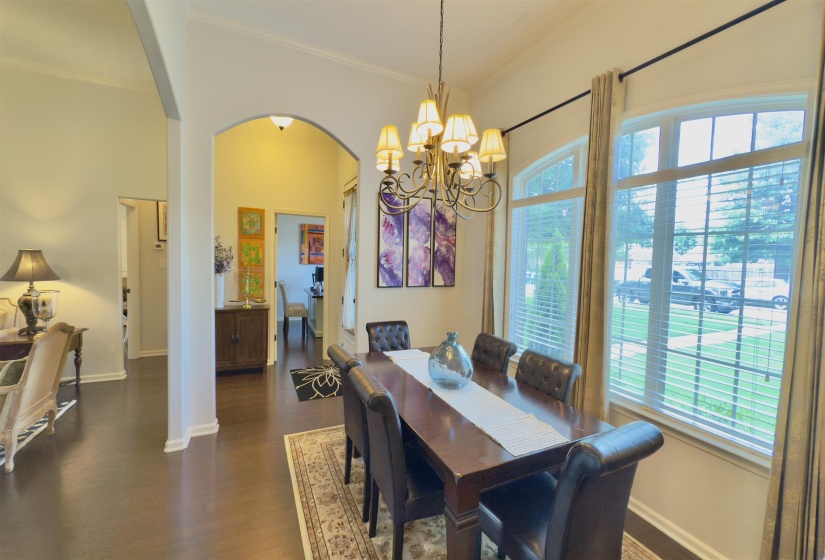 Dining area featuring arched walkways, healthy amount of natural light, ornamental molding, dark wood finished floors, and a chandelier