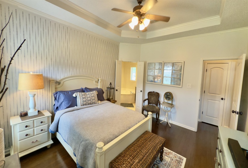 Bedroom with a tray ceiling, crown molding, dark wood-style floors, ensuite bathroom, and ceiling fan