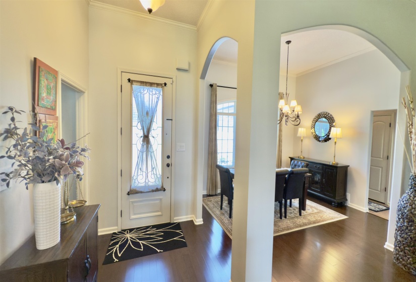 Entrance foyer with arched walkways, crown molding, dark wood-type flooring, and a chandelier