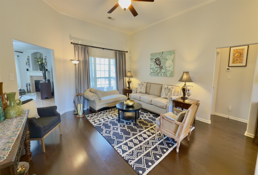 Living room with ceiling fan, wood finished floors, crown molding, and a fireplace