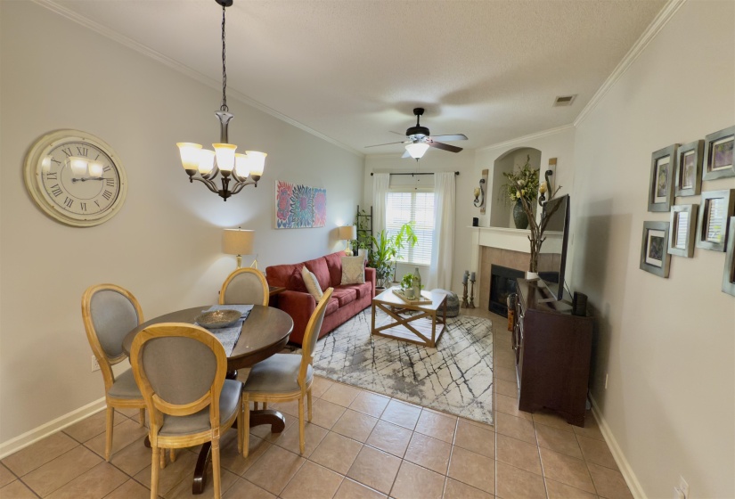 Living area featuring a tiled fireplace, ornamental molding, light tile patterned floors, a ceiling fan, and a chandelier
