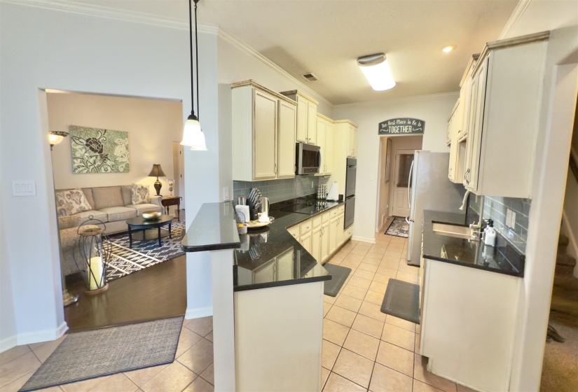 Kitchen featuring appliances with stainless steel finishes, a peninsula, dark countertops, backsplash, and ornamental molding