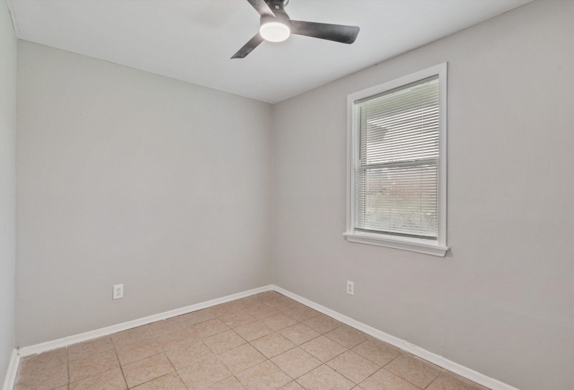 Light-filled room featuring neutral wall tones, tile flooring, a window with blinds, a ceiling fan with integrated lighting, and white baseboards