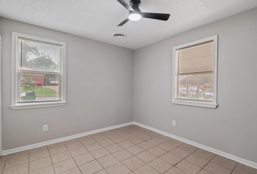 Room featuring light gray walls, tile flooring, two windows with blinds, a black ceiling fan, and white trim
